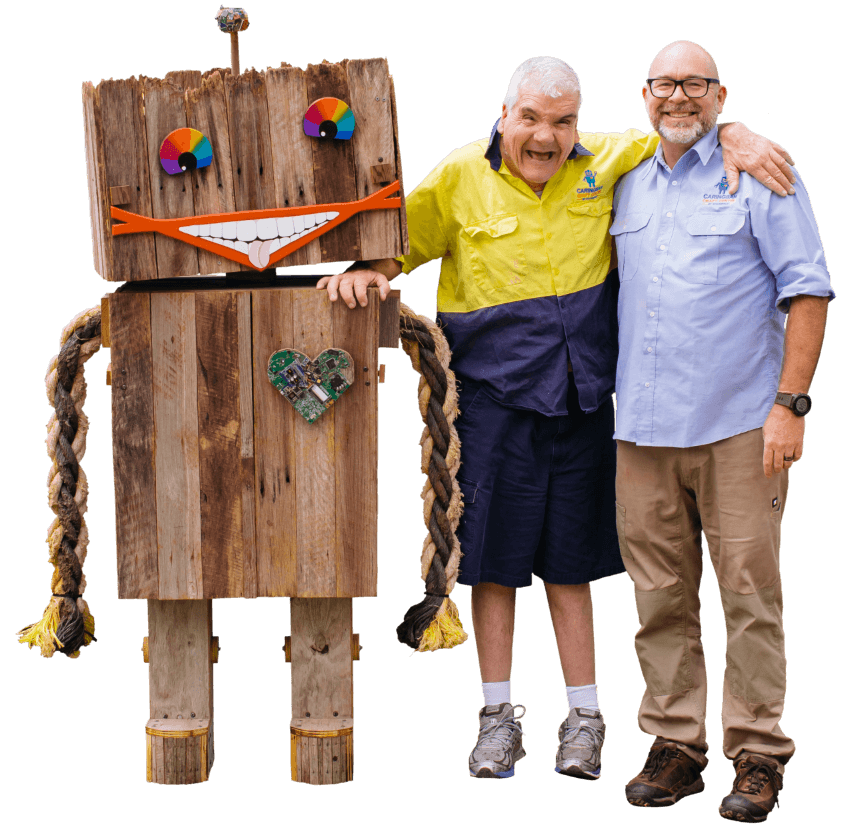 Two Men Smiling Standing Next To Wooden Robot Sculpture