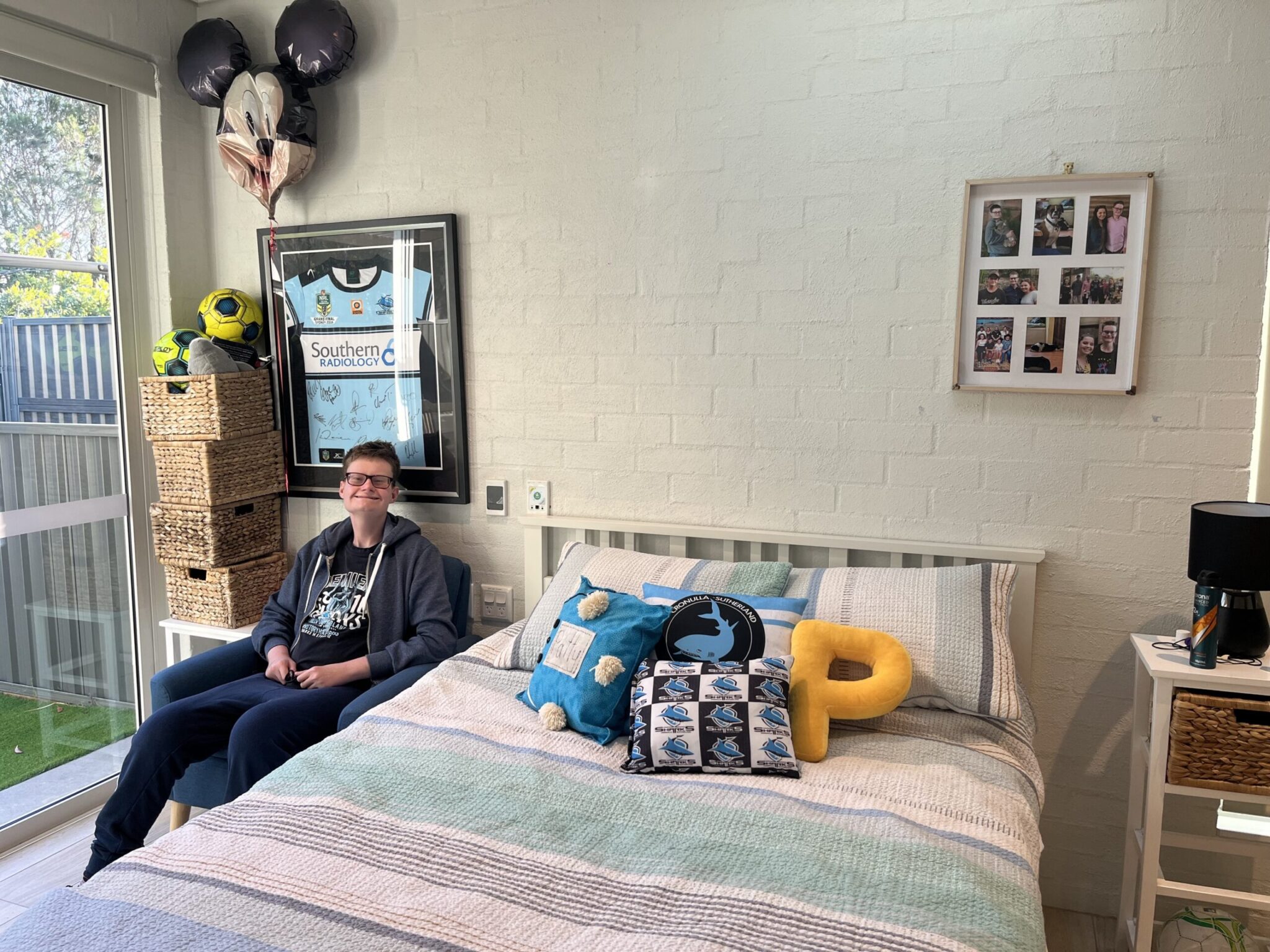 Patrick sitting in his neat and tody bedroom with his Cronulla Sharks themed decor.