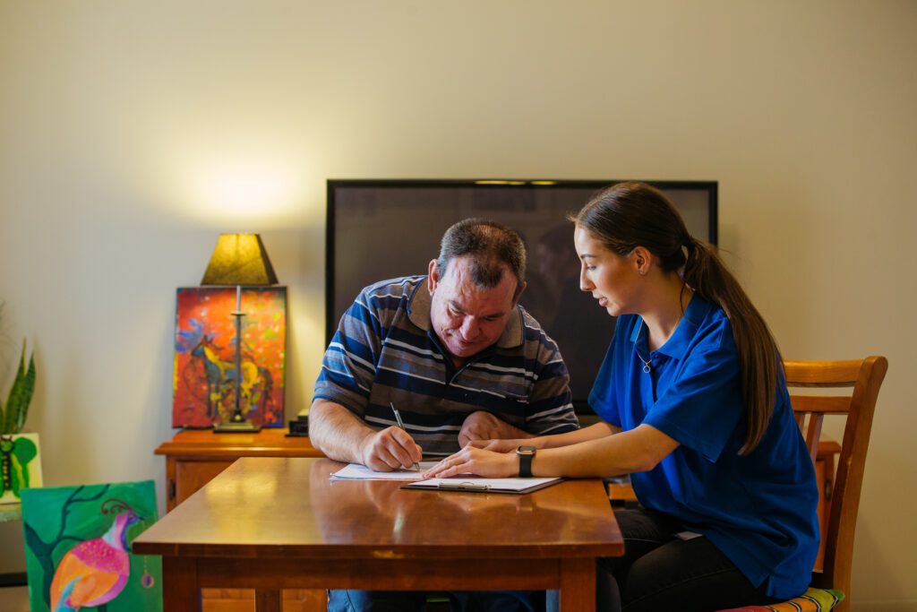 Participant writing on form with support worker watching on